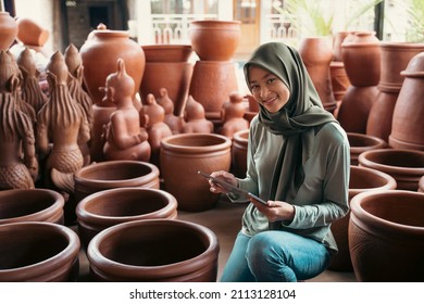 smiling woman in hijab holding a pad between the earthenware - Shutterstock ID 2113128104