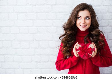 Smiling woman hold red gift box. Wall background. Concept of the New Year, Christmas and Valentine's Day.