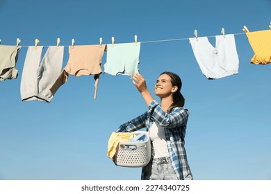 Smiling woman holding basket with baby clothes near washing line for drying against blue sky outdoors - Powered by Shutterstock