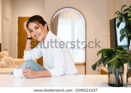 smiling woman holding coffee cup looking at camera. young woman drinking tea or cofffee in her kitchen while getting ready to go to work.