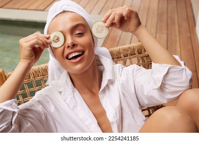 Smiling Woman Holding Cucumber Slices. Young Bathrobe Girl Having Fun at Street. Concept of Skincare - Powered by Shutterstock