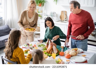 Smiling Woman Holding Delicious Pie Near Multicultural Family And Children During Thanksgiving Dinner