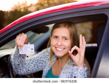 Smiling Woman Holding Her Driver License After Successful Driver's Exam In Her Red Car.