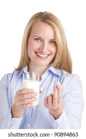 Smiling woman holding out a lactose intolerance tablet containing a lactase enzyme that will enable her to hydrolyze the lactose in her glass of milk.