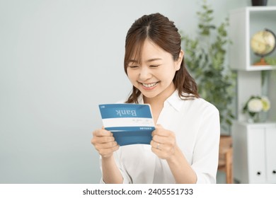 Smiling woman holding a savings passbook in her hand.The book in the woman's hand is a bank book with the name of a fictitious Japanese bank.