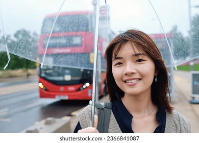 Smiling woman holding an umbrella on a rainy day with a bus in the background - Shutterstock ID 2366841087