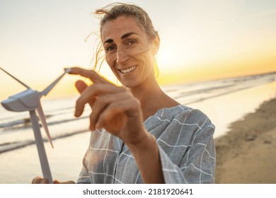 Smiling  Woman Holding Wind Turbine Model At Sunset On The Beach. Wind Turbines Windmill Energy Farm Concept Image