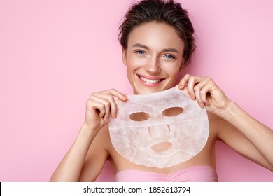 Smiling woman holds facial sheet mask. Photo of attractive woman with perfect skin on pink background. Beauty & Skin care concept - Shutterstock ID 1852613794