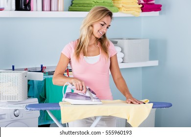 Smiling Woman Ironing Clothes Using Iron On Ironing Board After Laundry At Home