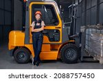 smiling woman labor worker near forklift driver in industry factory logistic shipping warehouse, posing with arms folded, dressed in uniform and orange protective hardhat, after successful good job