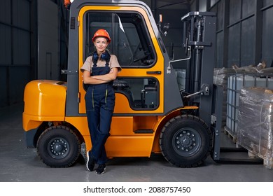 smiling woman labor worker near forklift driver in industry factory logistic shipping warehouse, posing with arms folded, dressed in uniform and orange protective hardhat, after successful good job - Shutterstock ID 2088757450