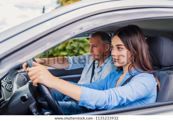 Smiling woman Learns to Drive in Car with\
instructor. Learning to Drive . Student driver taking driving test.\
Woman taking driving lessons from\
instructor