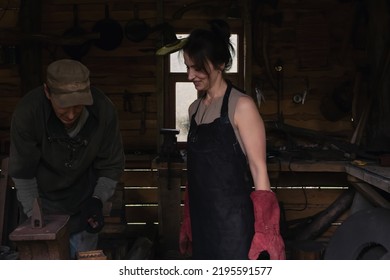 Smiling Woman In A Leather Work Apron And Large Mittens In An Old Forge