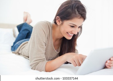 A Smiling Woman Lies On The Bed Scrolling Through Her Tablet.