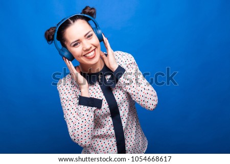Smiling woman listening to music through headphones on blue background in studio photo