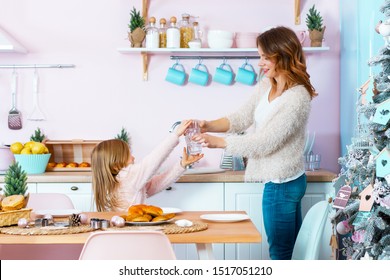 Smiling Woman And Little Cute Girl Are Cleaning Light Christmas Kitchen. Happy Mother And Daughter Are Serving Table With Dishes. Family Are Preparing For 
Festive Dinner, Celebration Of New Year.