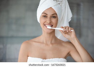 Smiling woman looking at camera, brushing teeth after showering, head shot close up. Happy healthy young lady feeling energetic after morning bath, using toothbrush, whitening teeth in bathroom. - Powered by Shutterstock