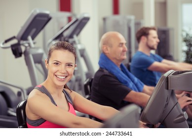 Smiling Woman Looking at Camera Using Recumbent Exercise Bike in Busy Gym - Powered by Shutterstock