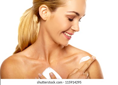 Smiling woman looking down applying body cream to her bare shoulder in a health and beauty concept