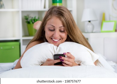 smiling  woman looking at her phone on the bed - Shutterstock ID 158757677