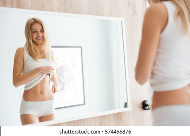 Smiling Woman Looking At Himself Near The Mirror And Showing Stomach