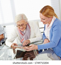 Smiling woman looks at a photo album with a happy elderly woman - Shutterstock ID 1749713204