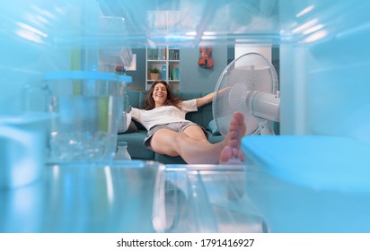 Smiling Woman Lying Down On The Sofa In Front Of The Open Fridge, She Is Keeping Herself Cool During The Summer