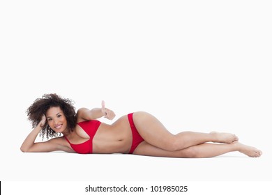 Smiling Woman Lying Down While Placing Her Thumbs Up Against A White Background