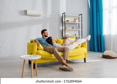 Smiling Woman Lying Near Handsome Man On Yellow Couch At Home