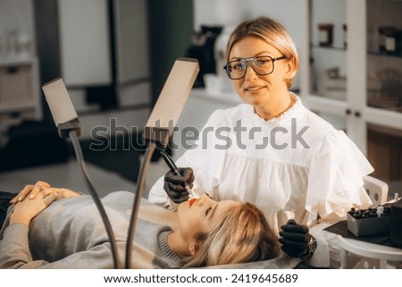 Smiling woman makes permanent makeup to another woman. High quality photo