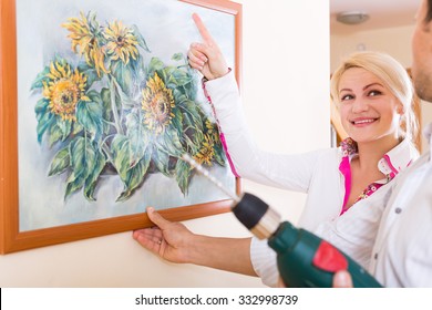 Smiling Woman And Man Hanging Art Picture In Frame On The Wall. Focus On Woman
