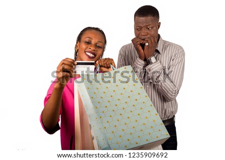 Smiling woman and a man standing and holding shopping bags and a credit card for online shopping or shopping. Man worries about his credit card being exhausted