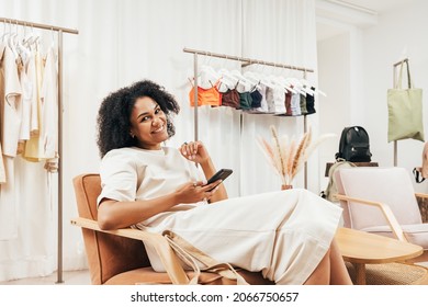 Smiling Woman With Mobile Phone Relaxing In Small Boutique And Looking At Camera