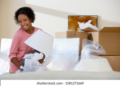 Smiling Woman Moving Into New Home Unpacking Lamp From Box