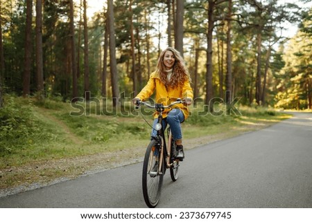 Smiling woman on a bicycle in an autumn park. Beautiful female tourist rides a bicycle, enjoys the sunny warm weather. Lifestyle, weekend concept. 