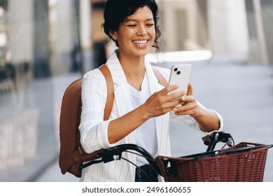 Smiling woman on a bicycle using her smartphone for texting while standing on the street. She appears happy and engaged with social media. - Powered by Shutterstock