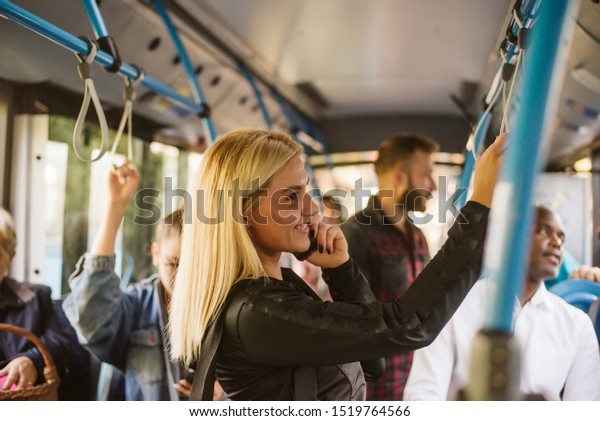 A smiling woman on a city bus. He holds the\
doorknob and talks on the\
phone