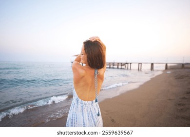 Smiling Woman on Sandy Beach at Sunset with Ocean Waves and Wooden Pier View - Powered by Shutterstock