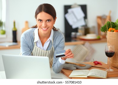 Smiling woman online shopping using computer and credit card in kitchen - Shutterstock ID 557081410