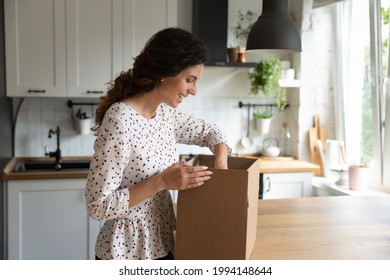 Smiling Woman Opening Box In Kitchen At Home, Satisfied Customer Received Parcel, Removing Package, Attractive Young Female Excited By Good Fast Delivery Service, Surprise Or Internet Order