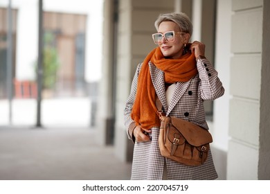 Smiling Woman Outdoor Portrait. Short blonde hair fashion model wears stylish clothes, double-breasted jacket, leather handbag, ochre knitted scarf and glasses. Fashion trend of autumn or spring - Shutterstock ID 2207045719
