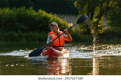 Smiling woman paddling a kayak on a serene river during golden hour. Kayak Water Sports concept image - Powered by Shutterstock