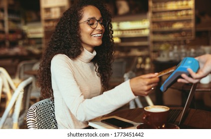 Smiling woman paying contactless using her credit card in a cafe to pay her bill. Female customer making a card payment in a restaurant. - Powered by Shutterstock