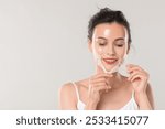 Smiling woman peeling off face mask on light grey background. Space for text