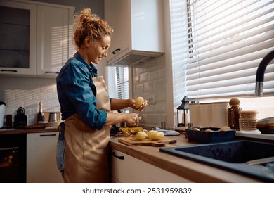 Smiling woman peeling potatoes while cooking for Thanksgiving at home. Copy space. - Powered by Shutterstock