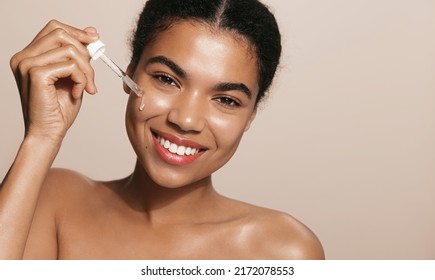 Smiling woman with perfect skin, applies tea trea, collagen face lifting serum, holds dropper, stands over brown background - Shutterstock ID 2172078553