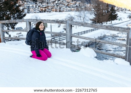 smiling woman in pink ski pants resting on the snow after playing with her children