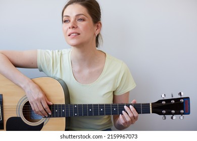 Smiling Woman Play On Guitar And Looking Away. Isolated Portrait On Gray Back.