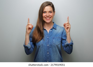 Smiling Woman Pointing Finger Up, Isolated Portrait On Gray Wall Background. Wide Smile With Teeth.