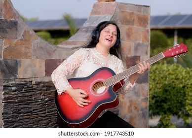 A smiling woman posing with guitar  outside